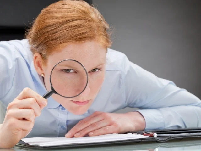 Mulher ruiva investigando com uma lupa se o certificado é válido.
